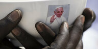 Eine Frau hält eine Tasse mit dem Konterfei von Papst Franziskus in der Hand