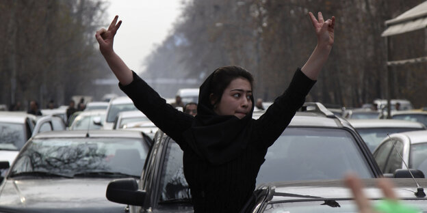 Eine junge Frau streckt ihre Arme mit Victory-Zeichen aus einem Autoconvoy