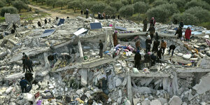 Rettungskräte stehen auf den Trümmern eingestürzter Häuser, im Hintergrund sind Olivenhaine zu sehen