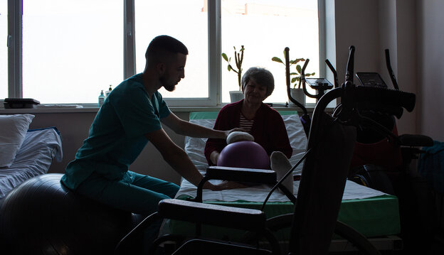 Ein Physiotherapeut behandelt eine Frau, die mit amputiertem Unterschenkel auf dem Bett sitzt