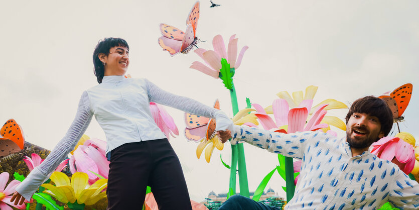 Derya Yildirim & Graham Mushnik tanzen vor einer bunt bemalten Wand mit Blumen und Schmetterlingen