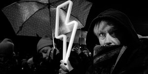 Schwarz-weiß-Aufnahme, eine Frau hält einen Blitz ,das Symbol für das Abtreibungsverbot in den Händen bei einer Demonstration