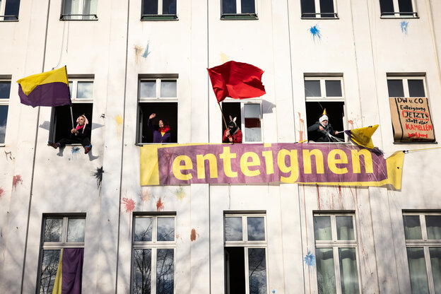 Aus geöffneten Fenstern eines Hauses werden Fahnen der Initiative 