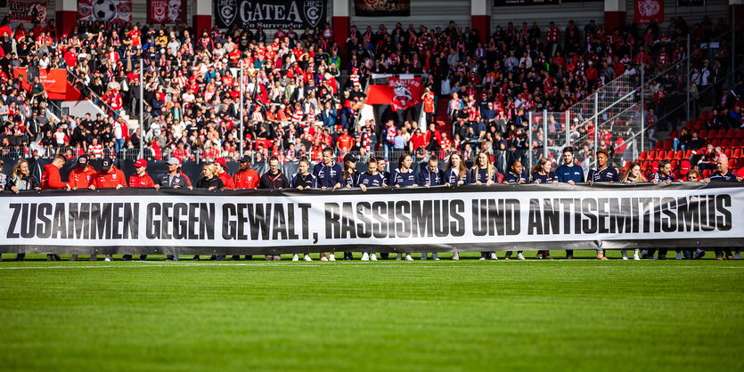 Tribüne in Fußballstadion, davor Transparent gegen Antisemitismus