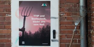 An der weißen Eisentür in einer rotverklinkerten Wand hängt ein Plakat. Darauf steht: TTIP und Gentechnik, bleibt uns vom Hof