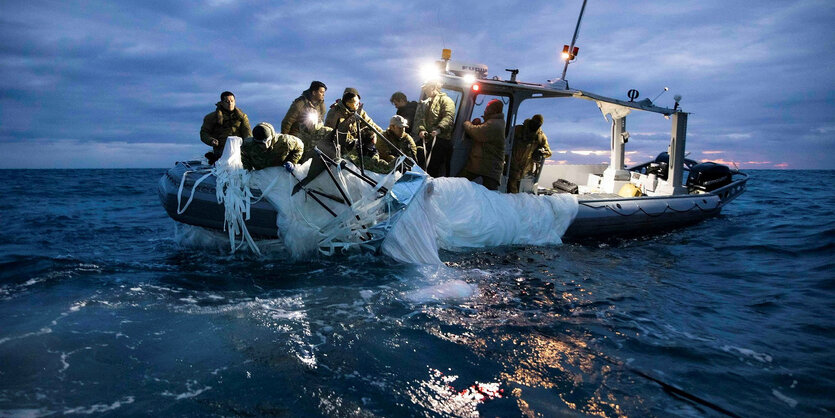 Personen auf einem Boot ziehen eine weiße Plane aus dem Wasser