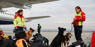 Eine Frau vom SAR-Team steht mit ihrem Hund, der ein Halsband mit der Aufschirft hope trägt und dem deutschen Wappen, vor einem Flugzeug