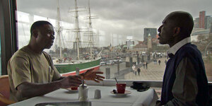 Zwei Männer an einem Tisch mit Blick auf einen Hafen