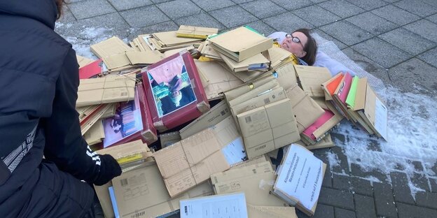 Eine Frau liegt auf dem vereisten Bürgersteig vor dem Berliner Rathaus unter Akten begraben.