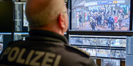 Ein Mann mit einer Polizeijacke sitzt vor Bildschirmen, auf denen Kamerabilder von Bahnsteigen zu sehen sind
