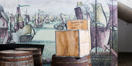 Auschnitt aus einer Ausstellung zu Hannovers kolonialer Geschichte, im Vordergrund sind Kisten und Fässer zu sehen, im Hintergrund Bilder von Schiffen