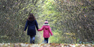 Eine Frau und ein Kind gehen auf einem mit Blättern bedecktem Waldweg spazieren