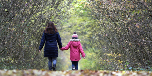 Eine Frau und ein Kind gehen auf einem mit Blättern bedecktem Waldweg spazieren