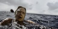 Ein Mann schwimmt mit panischem Gesichtsausdruck im Meer.