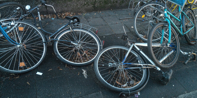 kaputte Fahrräder liegen auf dem Bordstein neben einem Fahrradständer