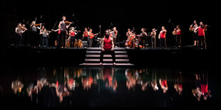 Orchestermusiker in schwarzen Hosen und roten shirts spiegeln sich auf einer dunklen Fläche