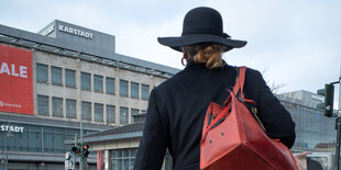 Eine Dame mit Hut und roter Tasche läuft richtung Karstadt am Hermannplatz