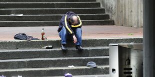 Ein schläft sitzend auf einer Treppe, daneben Bierflaschen