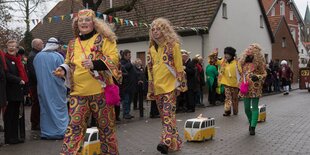 Menschen in Hippiekostümen ziehen Spielzeugautos hinter sich her