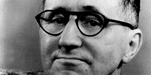 Portrait von Bertolt Brecht mit einer Brille, seine Lippen sind zusammengepresst