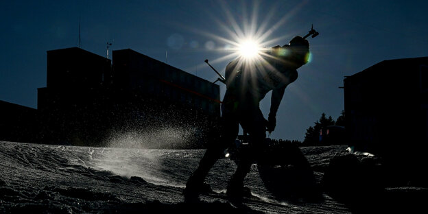 Eine Person fährt Ski, hinter ihm sind Gebäude, und am blauen Himmel scheint die Sonne