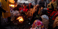 Menschen sitzen zwischen Trümmern an einem Feuer