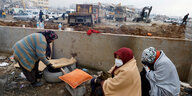 Drei Frauen sitzen in Decken gehüllt vor Trümmern