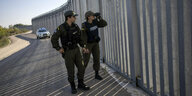 Ein Polizist und eine Polizistin laufen an einem Zaum aus Metall entlang. Die Frau blickt durch ein Fernglas