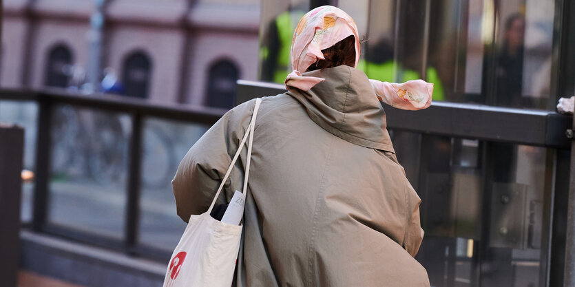 Der Wind bläst in Berlin den Mantel einer Frau auf und lässt ihr Halstuch wehen