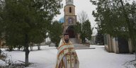 Ein Pfarrer steht im Schnee vor einer Kirche