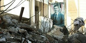 Ein Poster mit dem Portrait von Bashir-al-Assad ist hinter dem Schutt eines eingestürzten Hauses zu sehen
