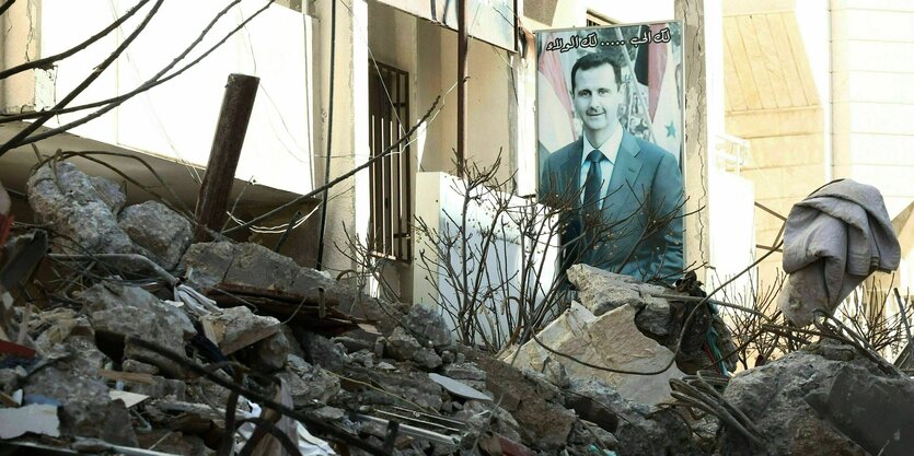 Ein Poster mit dem Portrait von Bashir-al-Assad ist hinter dem Schutt eines eingestürzten Hauses zu sehen