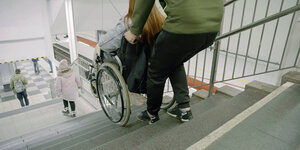 Eine Frau im Rollstuhl wirtd eine Treppe hinuntergebracht
