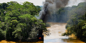 Rauchschwaden steigen aus Bäumen im Regenwald empor. Ebenfalls zu sehen ist der braune Amazonas-Fluss