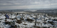 Kreuze auf frisch ausgehobenen Gräbern in einer von Schnee bedeckten Landschaft