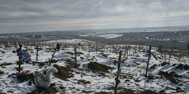 Kreuze auf frisch ausgehobenen Gräbern in einer von Schnee bedeckten Landschaft