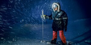 Julia Martin steht im Schnee, trägt eine Kopflampe und hält einen Stecken mit einer Sonde in der Hand.