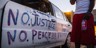 Auf einem Auto, in dem eine Frau sitzt, steht „No Justice, no peace", daneben steht ein Mann
