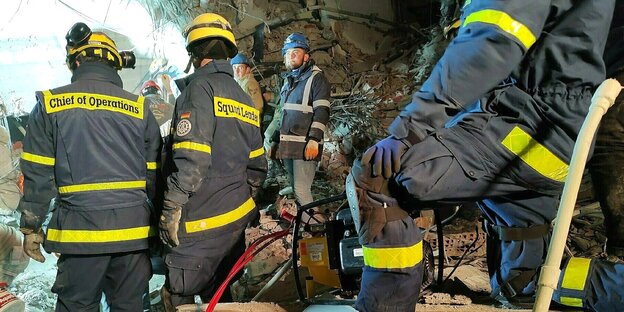 Vier Männer in der Uniform des THS stehen auf dem Schutt eines eingestürzten Hauses
