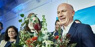 Kai Wegner steht lachend mit einem Blumenstrauß auf einer Bühne, umringt von Anhängern