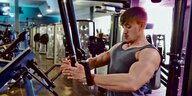 Ein junger Mann mit muskelbepacktem Oberkörper trainiert in einem Fitnessstudio.
