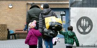 Eine Familie, gesehen von hinten, geht auf ein Haus zu