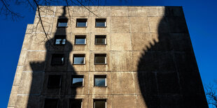 Ein Plattenbau vor blauen Himmel. Auf dem Gebäude sieht man den Schatten eines Kirchturms.