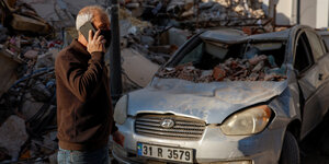 Eine Person telefoniert vor einem zerstörten Haus