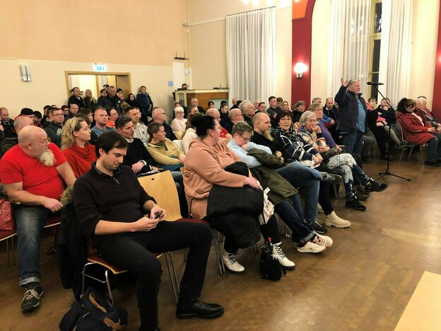 Menschen sitzen in Stuhlreihen in einem Raum, ein Man steht in der Mitte und spricht