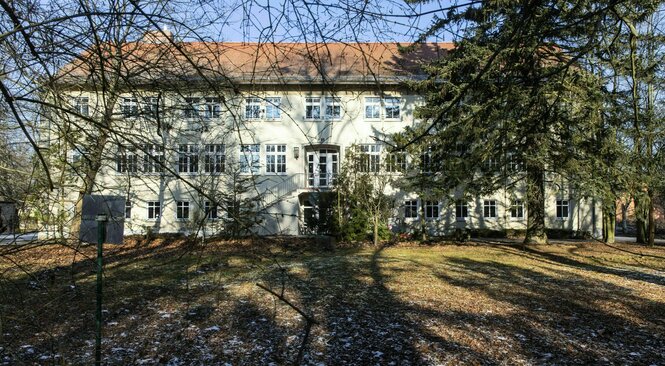 Die Flüchtlingsunterkunft in Biesenthal, ein langgestreckter heller Bau umgeben von Bäumen