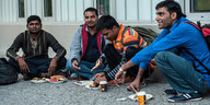 Männliche Flüchtlinge sitzen auf dem Bürgersteig und essen