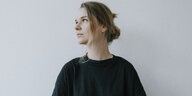 Porträtfotografie: Die Cellistin Dobrawa Czocher steht vor einer hellen Wand, sie trägt einen schwarzen Pullover und blickt nach links