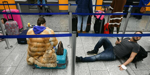 Wartende Passagiere am Flughafen sitzen und liegen auf dem Boden