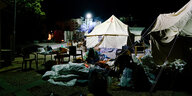 Menschen sitzen in Decken gehüllt nachts vor Zelten